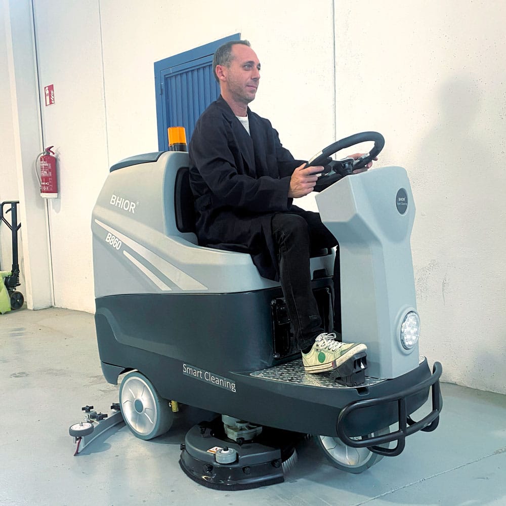 Operario de fregadora industrial b860 de conductor sentado limpiando almacén.